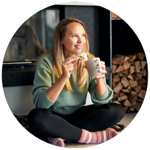 Junge Frau isst einen Keks mit Sahne im Schneidersitz vor dem Kamin