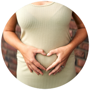 Schwangere Frau im hellgrünen Rippkleid formt ein Herz mit ihren Händen vor ihrem Bauch