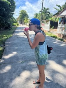 Frau mit Capy und Sonnenbrille isst einheimisches Eis auf La Digue (Seychellen). Das Eis besteht aus einem gefrorenen pürierten Früchten in einem Beutel.