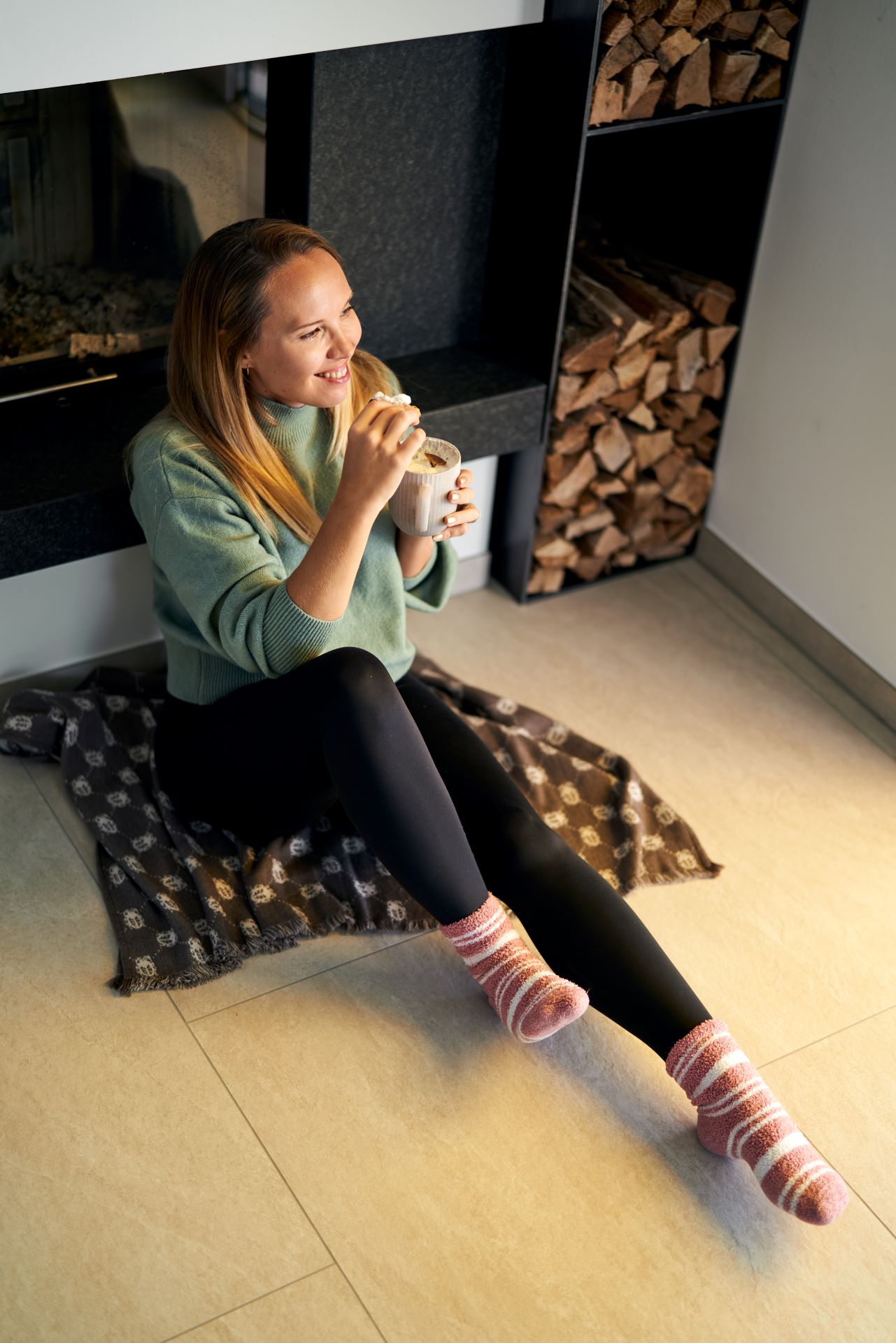 Frau vor Kamin isst einen Kecks mit heißer Schokolade