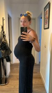 Selfie Frau mit Babybauch im schwarzen Trägerkleid (9. Monat)