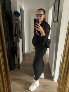 Selfie Frau mit Babybauch im schwarzen Rippkleid (6. Monat)